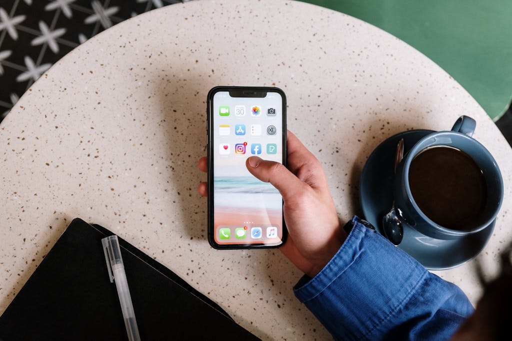 Person scrollt am Handy für Social-Media-Marketing und sitzt dabei an einem Tisch mit Kaffee